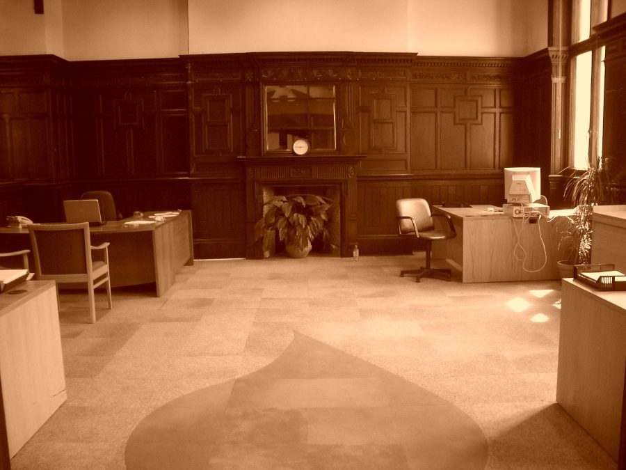 The fireplace wall of a large panelled room, with a leaf or spade shape set into the carpet tiles in front of it.
